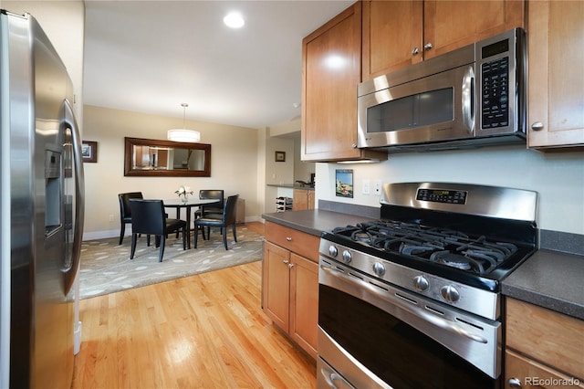 1544 Cottonwood Ave, Lafayette, CO 80026 - kitchen featuring baseboards, light wood finished floors, stainless steel appliances, hanging light fixtures, and dark countertops