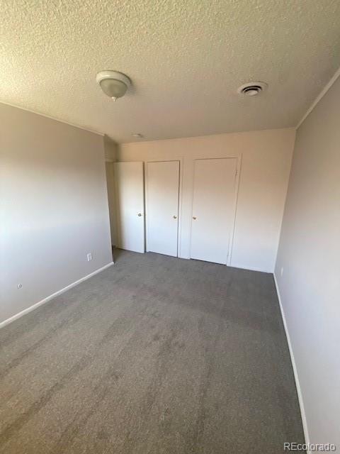 unfurnished bedroom with dark colored carpet, a textured ceiling, and two closets