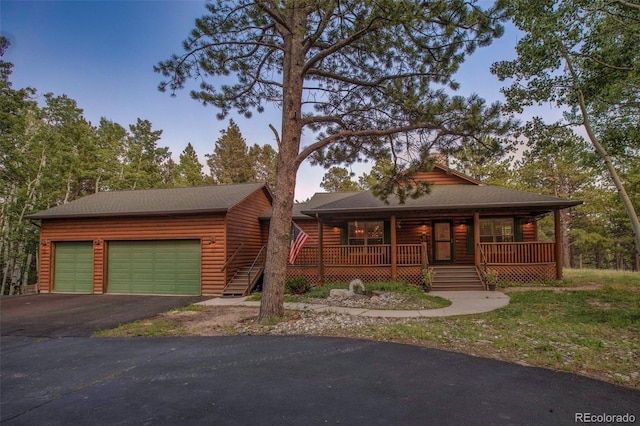 view of front facade with covered porch, log veneer siding, driveway, and an attached garage