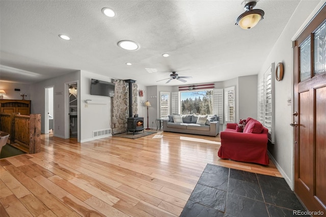 living room with a textured ceiling, wood finished floors, visible vents, baseboards, and a wood stove