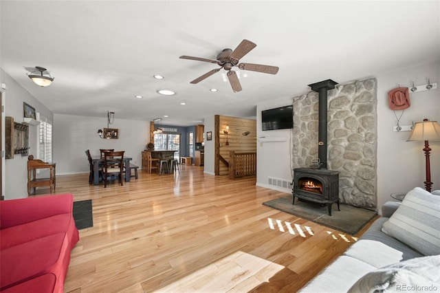 living room with recessed lighting, visible vents, a ceiling fan, a wood stove, and wood finished floors