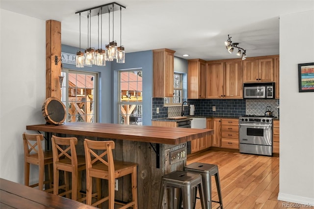 kitchen with decorative backsplash, dark countertops, a breakfast bar, hanging light fixtures, and stainless steel appliances