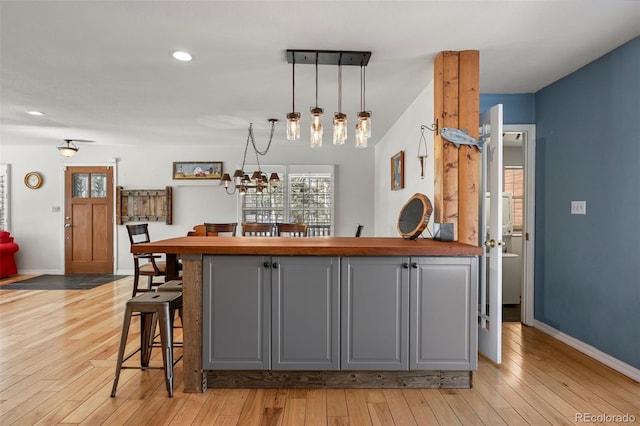 kitchen with a breakfast bar area, gray cabinetry, baseboards, light wood finished floors, and decorative light fixtures