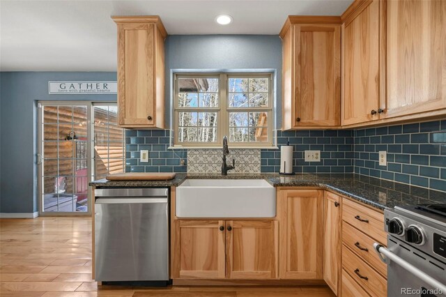 kitchen with stove, a sink, decorative backsplash, dishwasher, and dark stone countertops