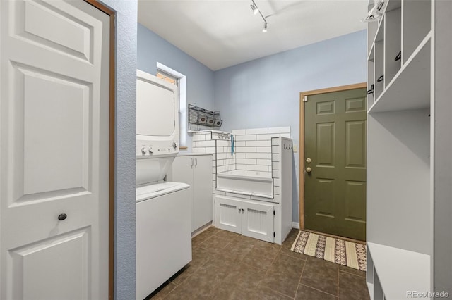 washroom with laundry area, dark tile patterned floors, stacked washer / dryer, and rail lighting