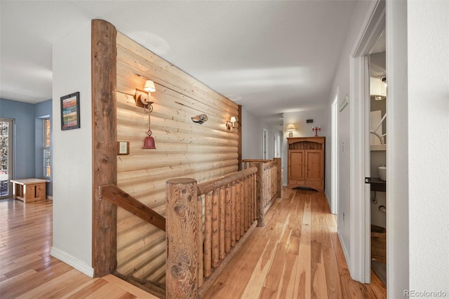 hall with rustic walls, baseboards, light wood finished floors, and an upstairs landing