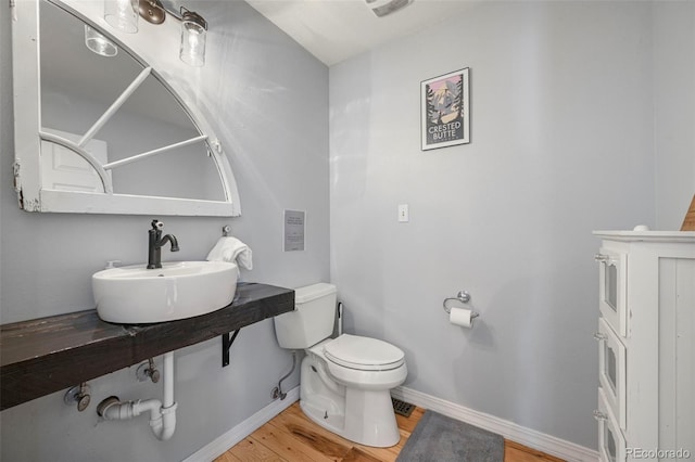 half bath with baseboards, a sink, toilet, and wood finished floors