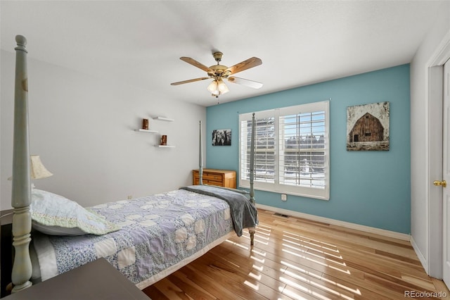 bedroom with ceiling fan, wood finished floors, visible vents, and baseboards