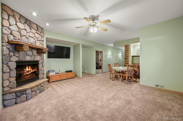 living room featuring a stone fireplace, light colored carpet, visible vents, baseboards, and a ceiling fan