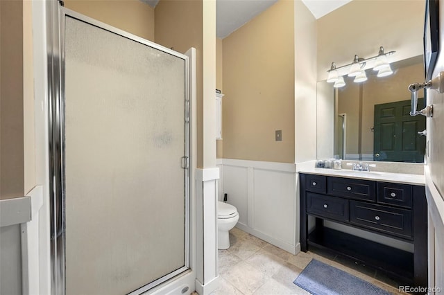 bathroom with a stall shower, toilet, a wainscoted wall, vanity, and a decorative wall