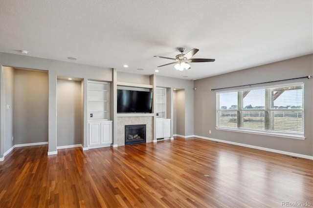 unfurnished living room featuring a tile fireplace, ceiling fan, baseboards, and wood finished floors