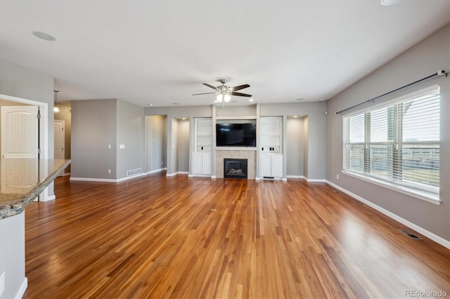 unfurnished living room featuring baseboards, visible vents, a fireplace, and light wood finished floors