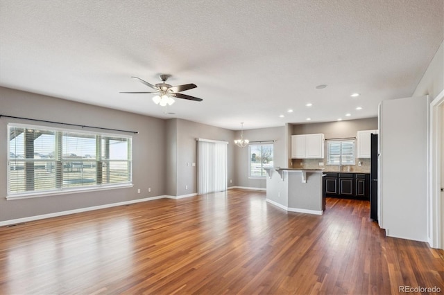 interior space with white cabinets, open floor plan, dark wood-type flooring, a kitchen bar, and backsplash