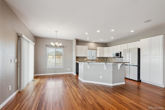 kitchen featuring stainless steel microwave, freestanding refrigerator, white cabinetry, wood finished floors, and a kitchen breakfast bar