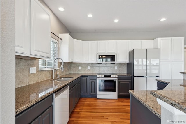 kitchen with light wood finished floors, appliances with stainless steel finishes, stone counters, and a sink