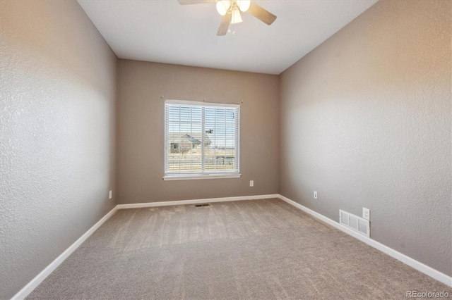 carpeted empty room featuring a ceiling fan, visible vents, a textured wall, and baseboards