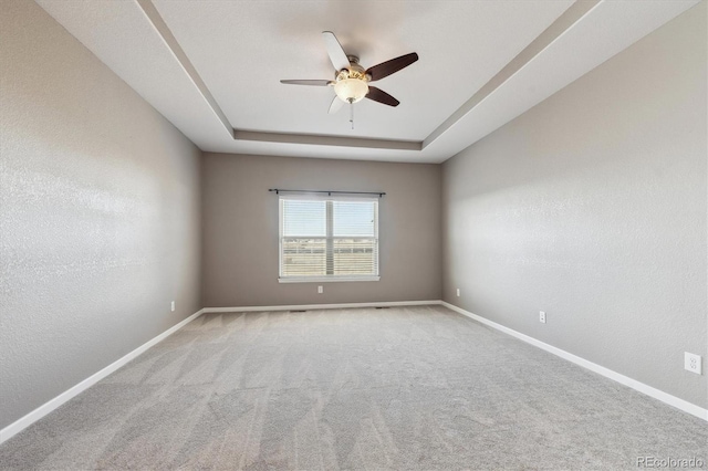 carpeted spare room featuring baseboards, a raised ceiling, a ceiling fan, and a textured wall