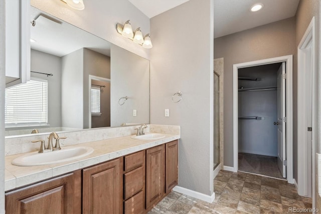 full bathroom with double vanity, a stall shower, a sink, and a walk in closet