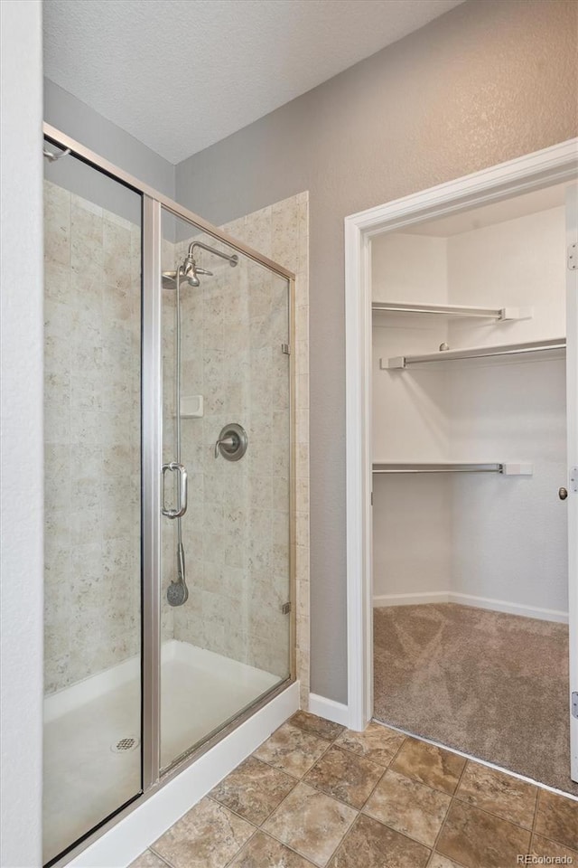 bathroom featuring a stall shower, baseboards, a walk in closet, and a textured ceiling