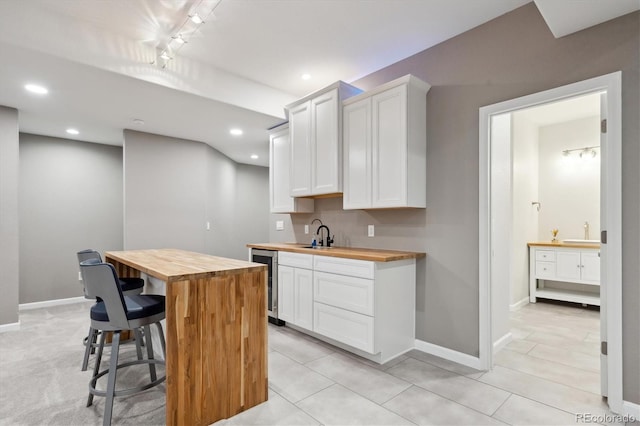 kitchen featuring wine cooler, a breakfast bar, wood counters, baseboards, and white cabinets