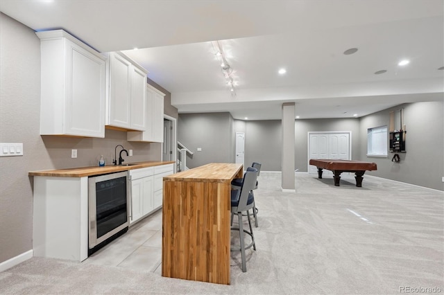 kitchen featuring beverage cooler, light colored carpet, wood counters, and white cabinets