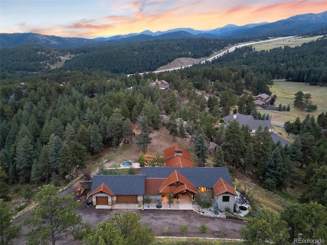 aerial view at dusk featuring a mountain view and a view of trees