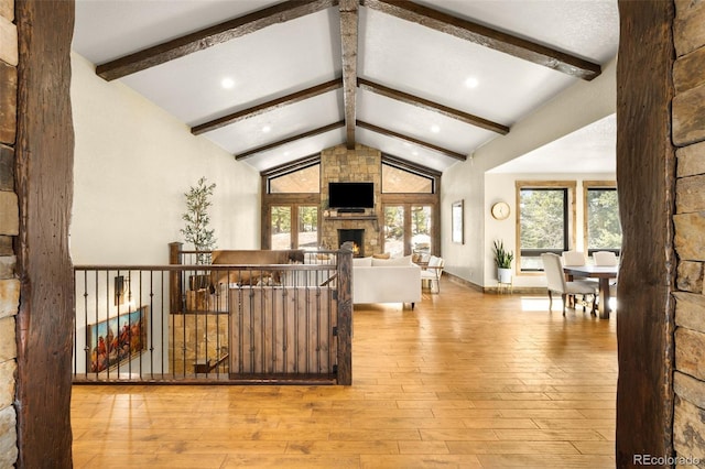 interior space with beam ceiling, a stone fireplace, high vaulted ceiling, and hardwood / wood-style flooring