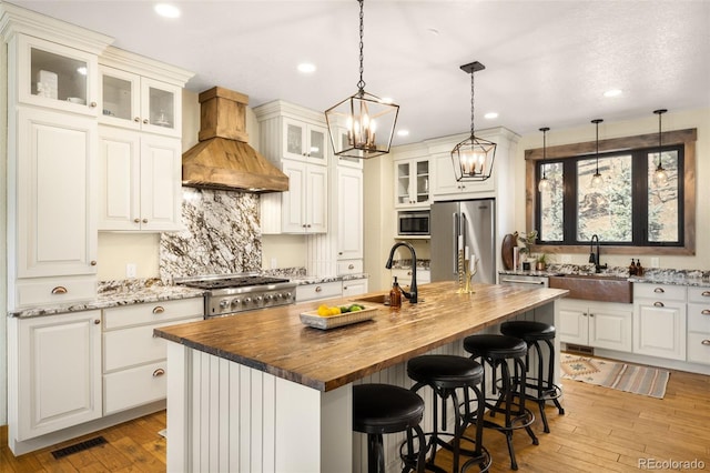 kitchen featuring custom exhaust hood, butcher block countertops, appliances with stainless steel finishes, and a sink