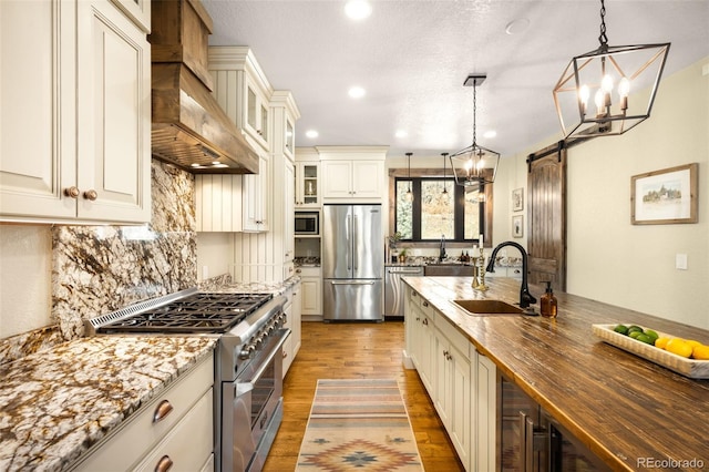 kitchen with a sink, wood counters, appliances with stainless steel finishes, an inviting chandelier, and light wood finished floors