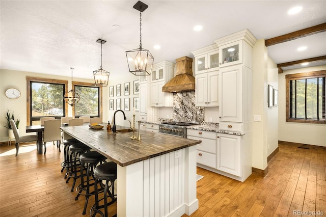 kitchen featuring premium range hood, a sink, decorative backsplash, stainless steel range, and light wood-style floors