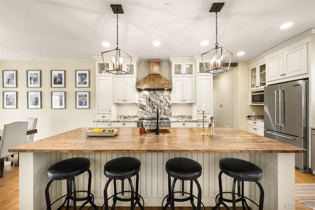 kitchen with premium range hood, butcher block countertops, light wood-type flooring, appliances with stainless steel finishes, and an inviting chandelier