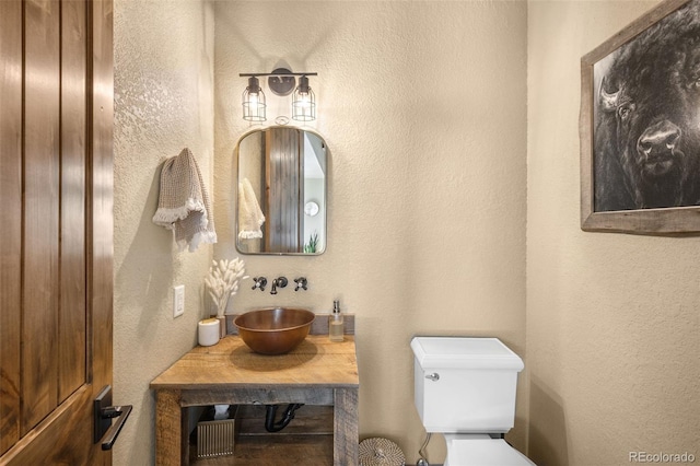 bathroom featuring toilet, vanity, and a textured wall