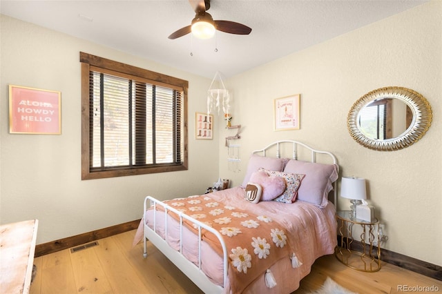 bedroom with ceiling fan, wood finished floors, visible vents, and baseboards