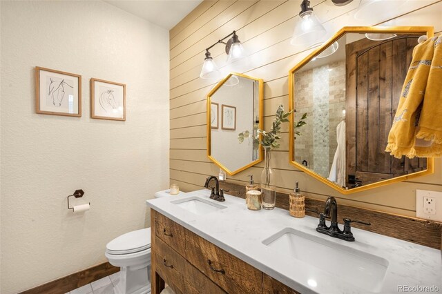 bathroom with double vanity, wooden walls, toilet, and a sink