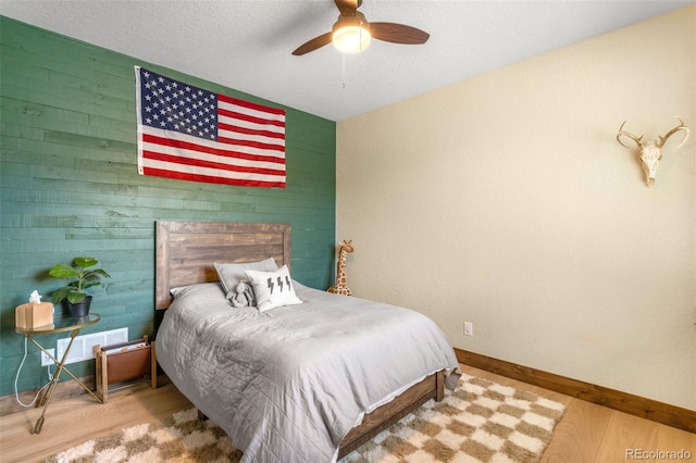 bedroom with visible vents, wood finished floors, wooden walls, baseboards, and ceiling fan