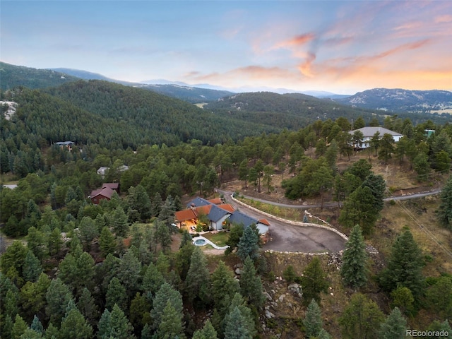 aerial view at dusk featuring a mountain view and a view of trees