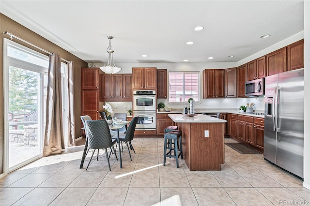 kitchen featuring a breakfast bar area, decorative light fixtures, light tile patterned floors, a center island, and stainless steel appliances