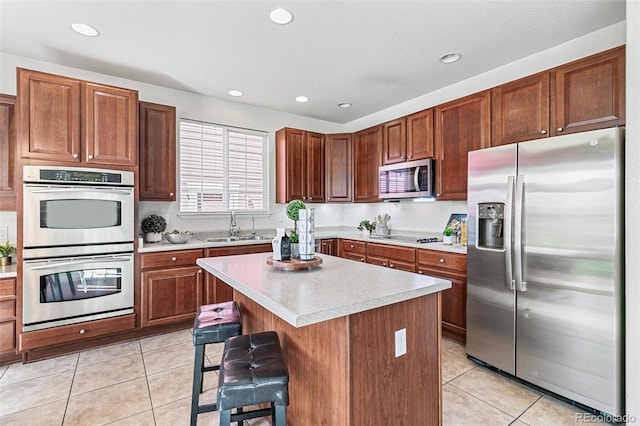 kitchen with appliances with stainless steel finishes, sink, light tile patterned flooring, a kitchen breakfast bar, and a kitchen island