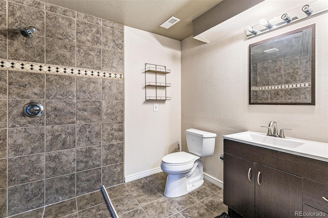 bathroom featuring toilet, tile patterned flooring, vanity, a textured ceiling, and tiled shower