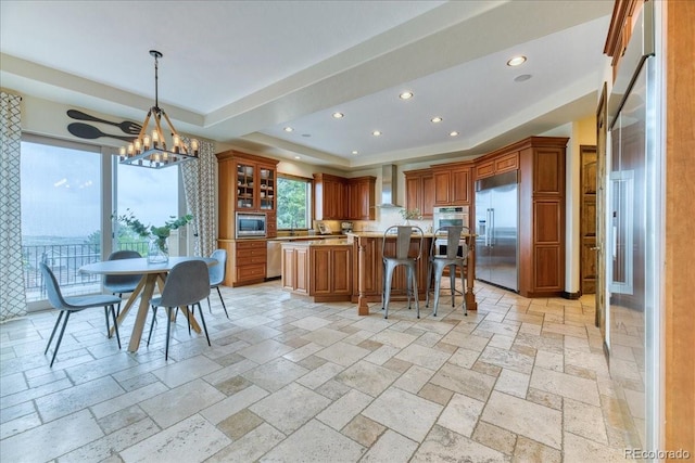 16713 W Archer Ave, Golden, CO 80401 - kitchen with built in appliances, a raised ceiling, wall chimney range hood, stone tile floors, and brown cabinetry
