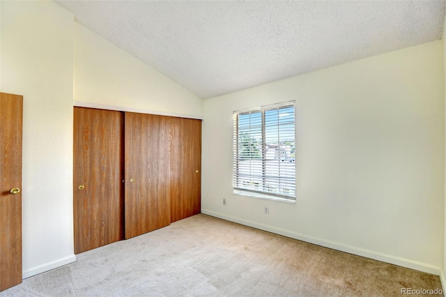 unfurnished bedroom featuring light colored carpet, lofted ceiling, a textured ceiling, and a closet