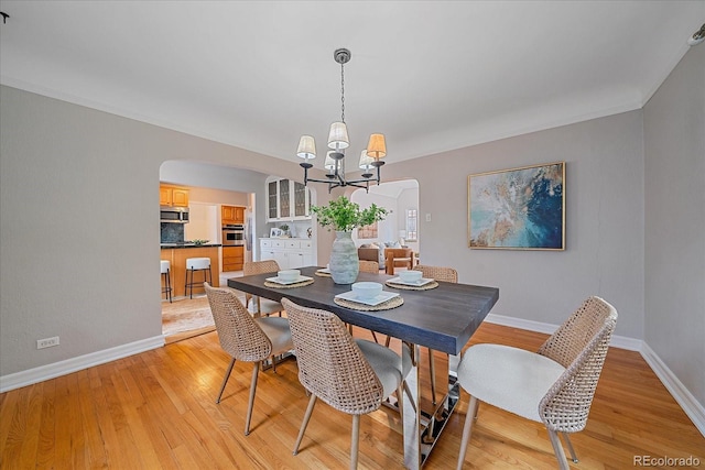 2065 Leyden St, Denver, CO 80207 - dining area featuring arched walkways, a chandelier, light wood-style flooring, baseboards, and crown molding