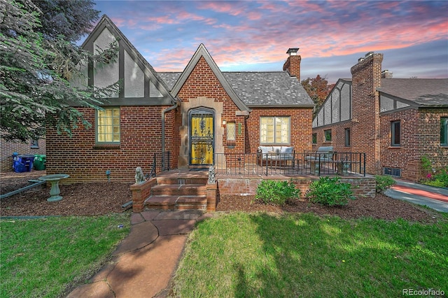 2065 Leyden St, Denver, CO 80207 - tudor house with brick siding, a chimney, a front yard, and roof with shingles