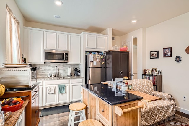 16043 Fillmore St, Thornton, CO 80602 - kitchen with appliances with stainless steel finishes, a kitchen bar, wood finished floors, tasteful backsplash, and white cabinetry