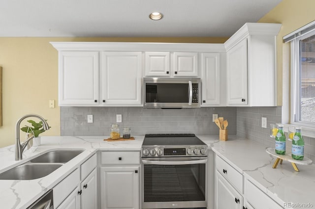 kitchen with appliances with stainless steel finishes, decorative backsplash, a sink, and white cabinets