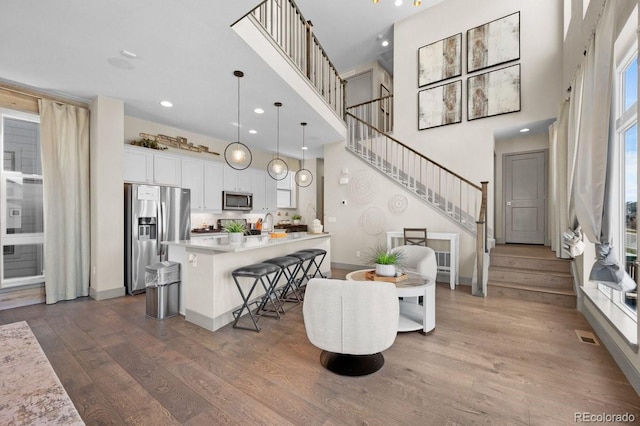 kitchen featuring appliances with stainless steel finishes, a kitchen breakfast bar, pendant lighting, hardwood / wood-style flooring, and white cabinetry