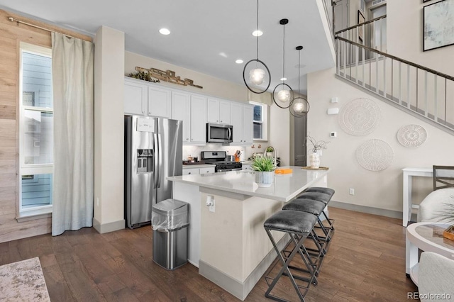 kitchen featuring appliances with stainless steel finishes, dark hardwood / wood-style flooring, a breakfast bar, decorative light fixtures, and white cabinets