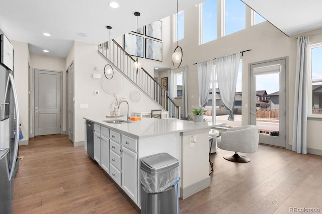 kitchen with white cabinetry, hanging light fixtures, a kitchen island with sink, appliances with stainless steel finishes, and light wood-type flooring