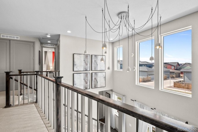 hall featuring light colored carpet and an inviting chandelier