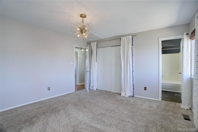 unfurnished bedroom featuring ensuite bathroom, a closet, a chandelier, and carpet flooring